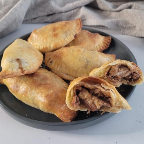 Cross section of Filipino empanada on a gray plate with other empanadas