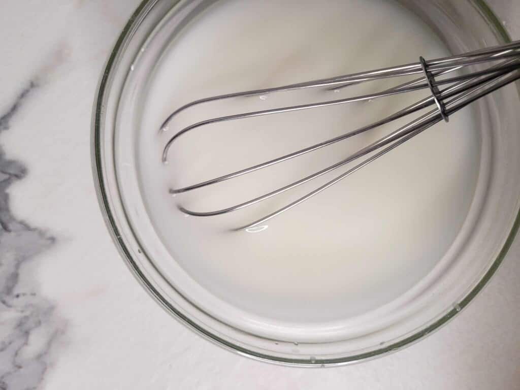 Cornstarch slurry in a clear bowl with a small whisk