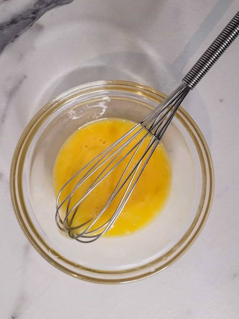 Whisked eggs yolks in a glass bowl with a small whisked