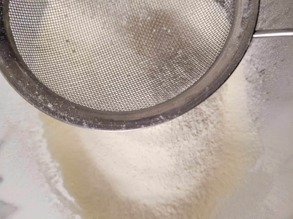 Sifted flour in the background with a sieve in the foreground