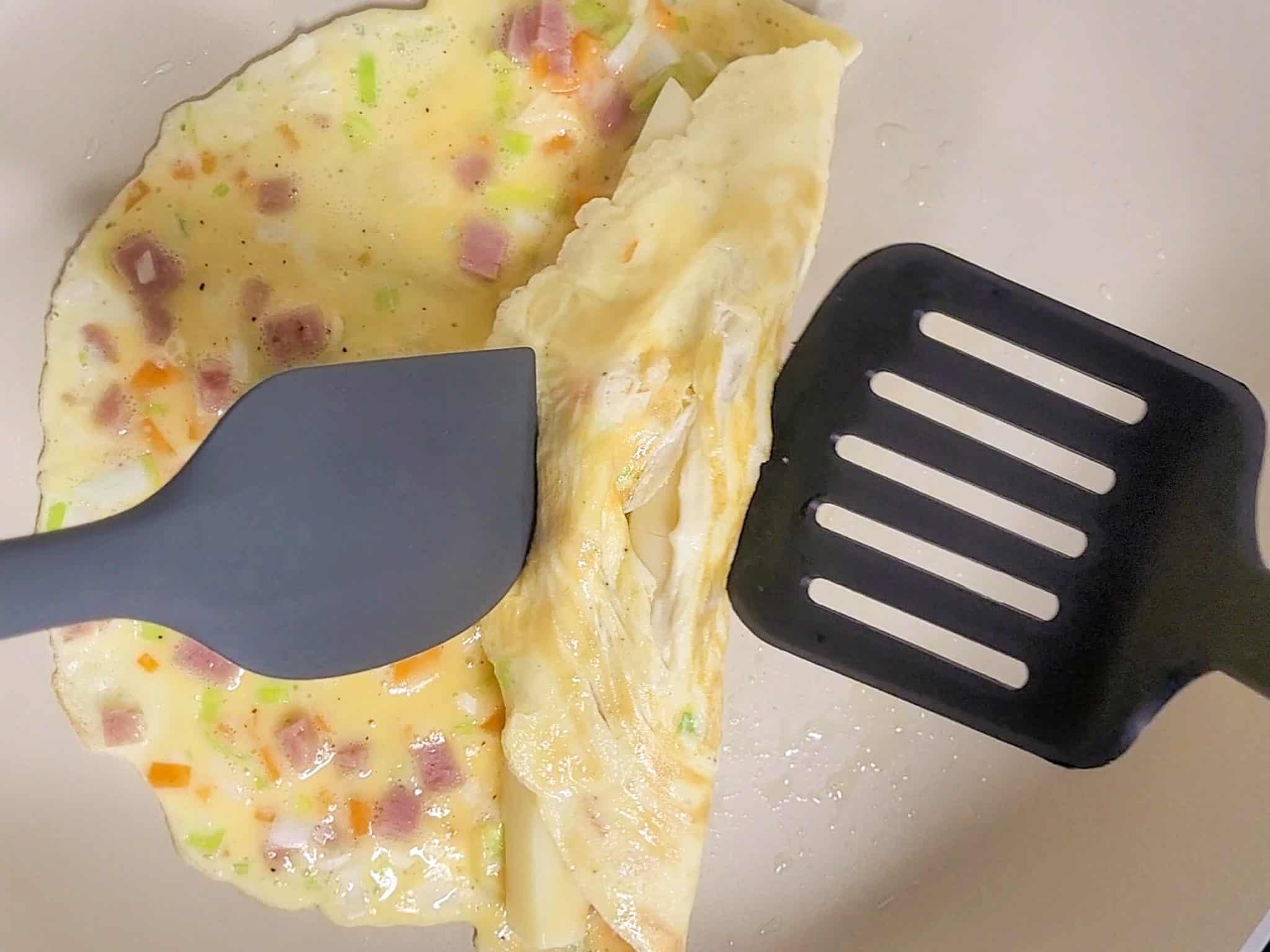 Two spatulas rolling an egg omelet