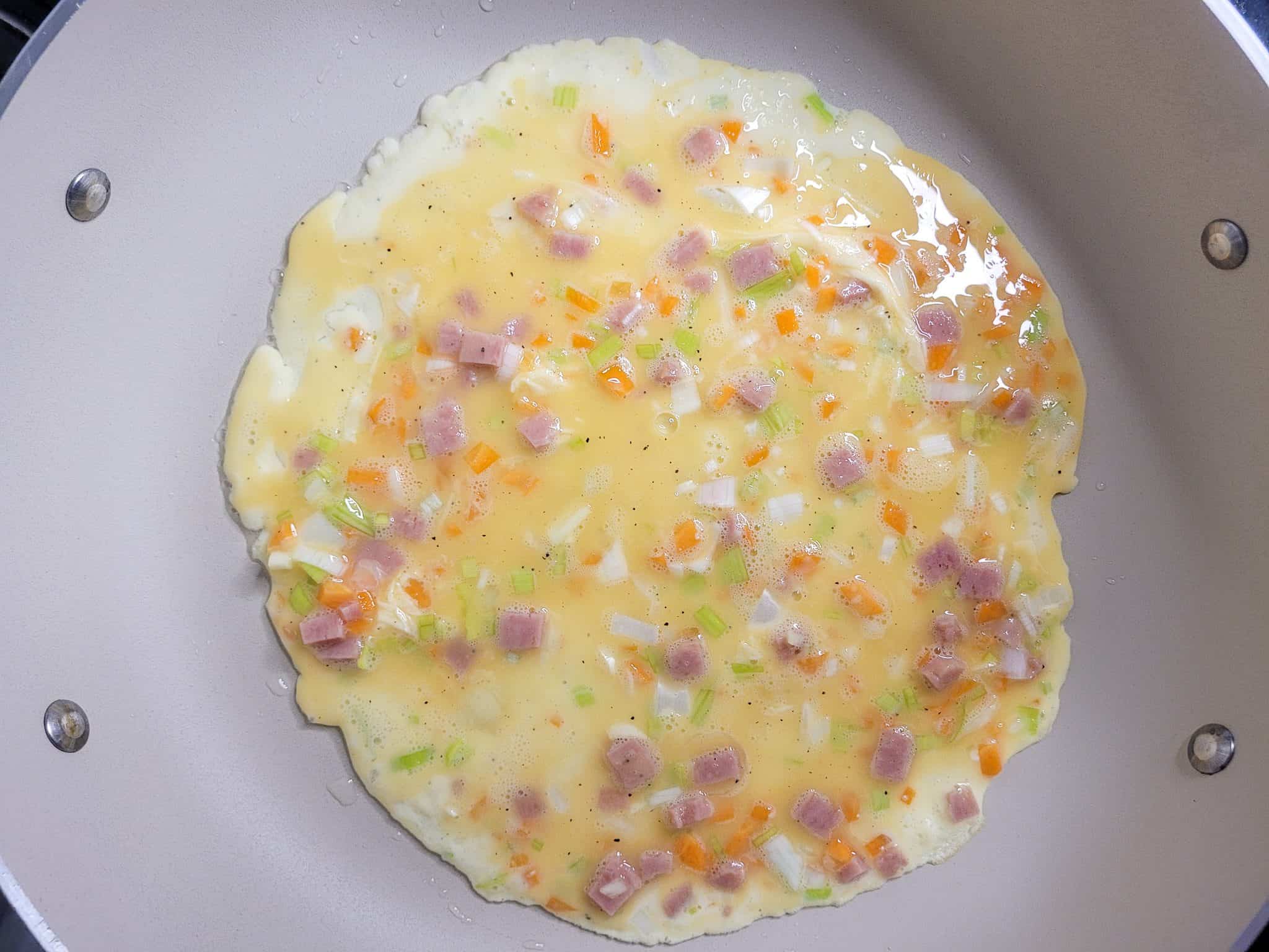 Raw eggs with vegetables and ham in a pan