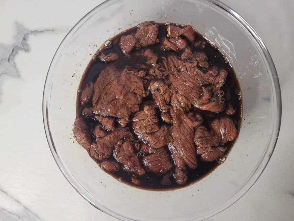 Marinated beef slices in a glass bowl on a marble countertop