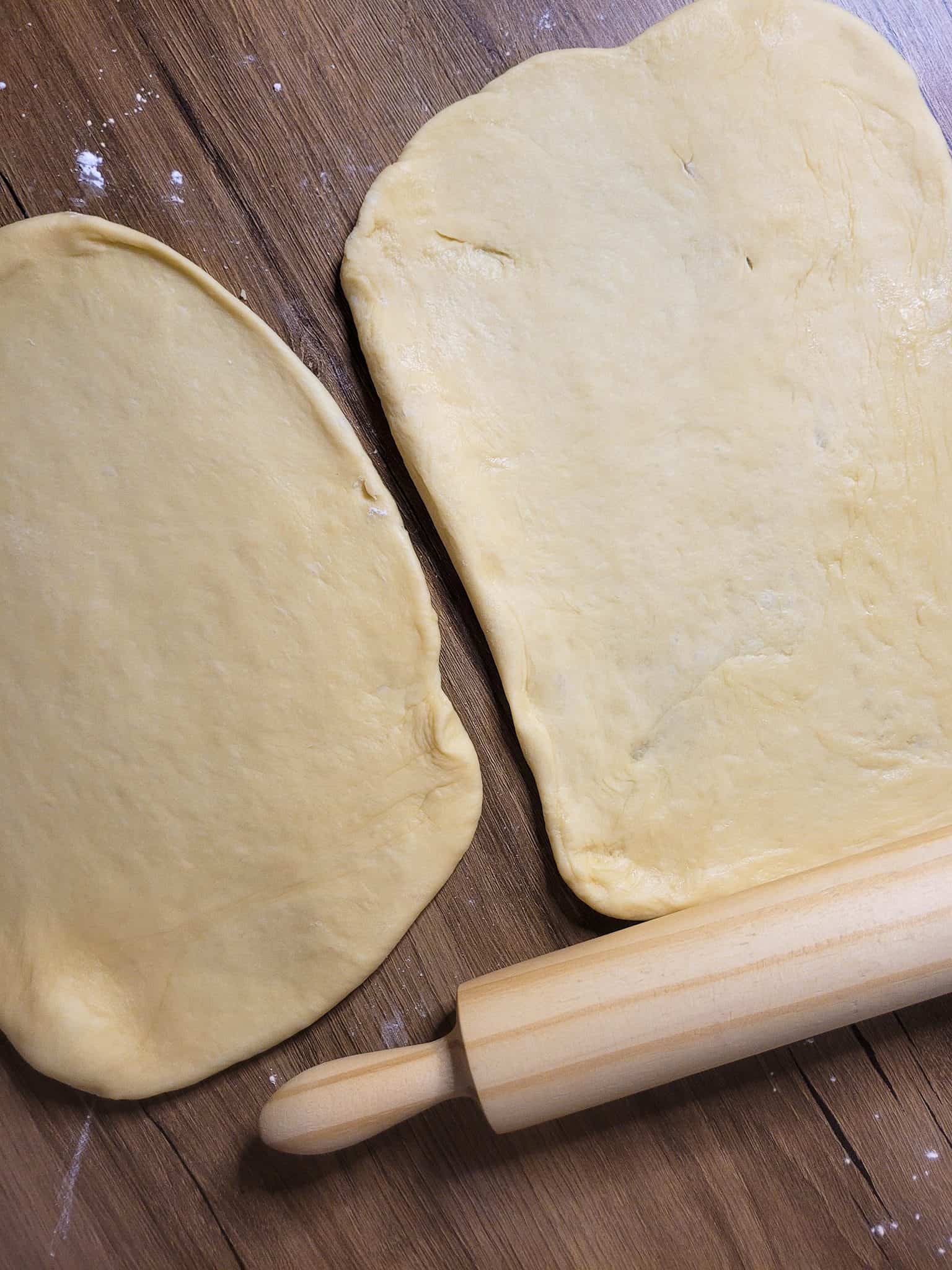 Rolled and flattened pieces of proofed dough next to a rolling pin