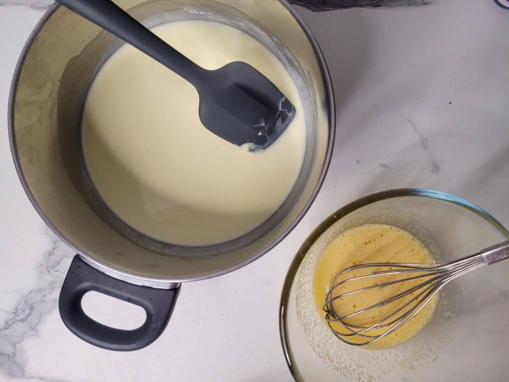 A pot with melted chocolate next to a bowl with whisked egg yolks