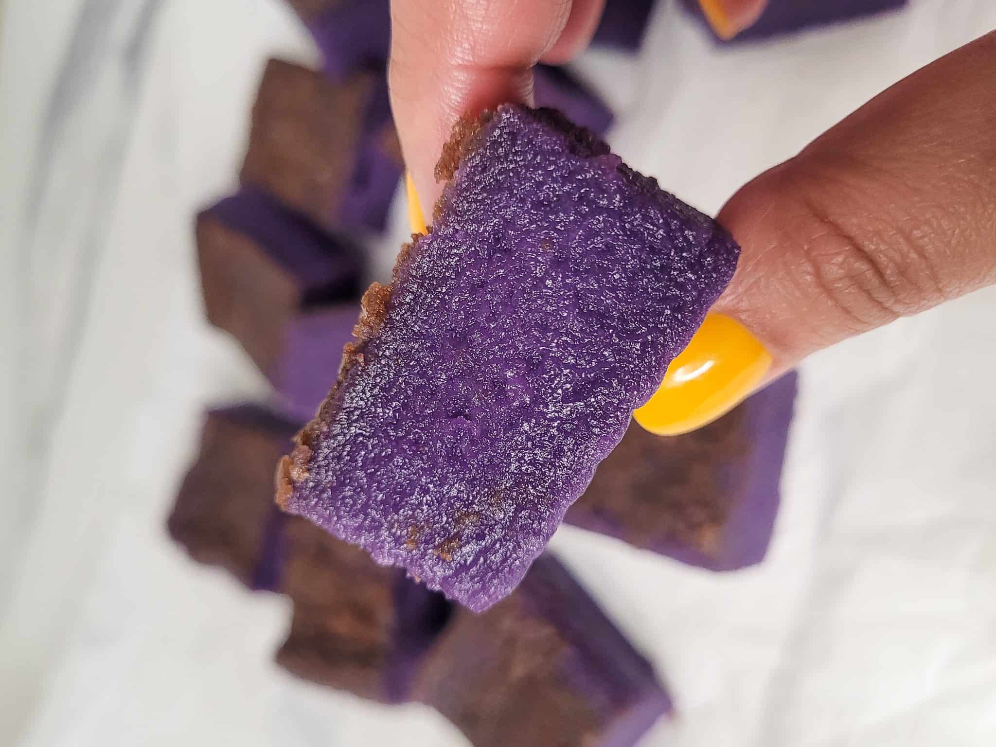 Fingers holding a piece of ube butter mochi