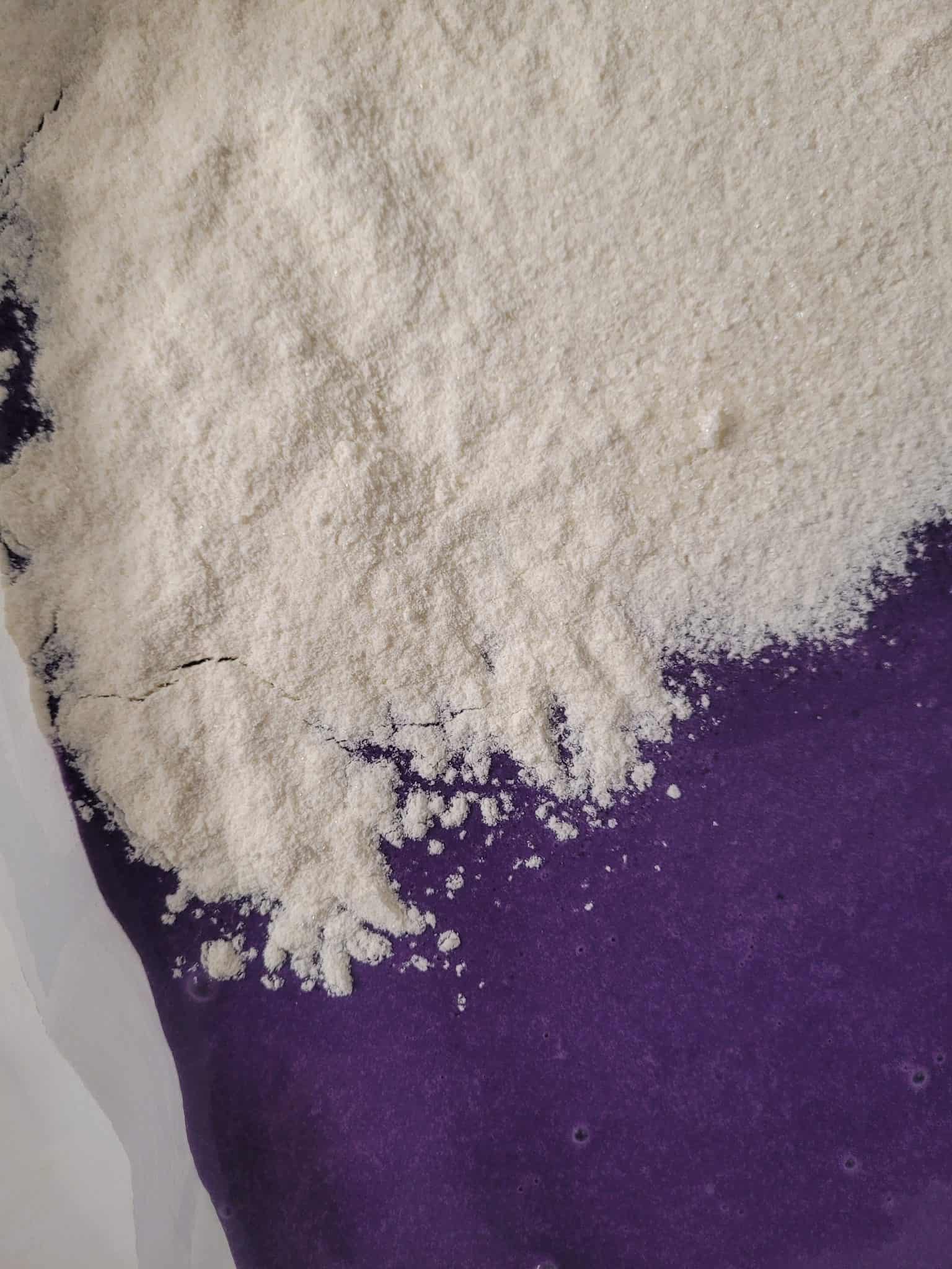 Dry cake mix on top of raw ube crunch cake batter in baking dish