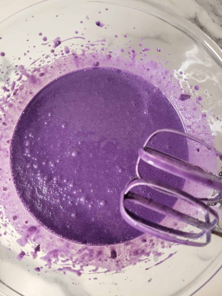 raw ube crunch cake batter in a glass bowl beneath egg beater