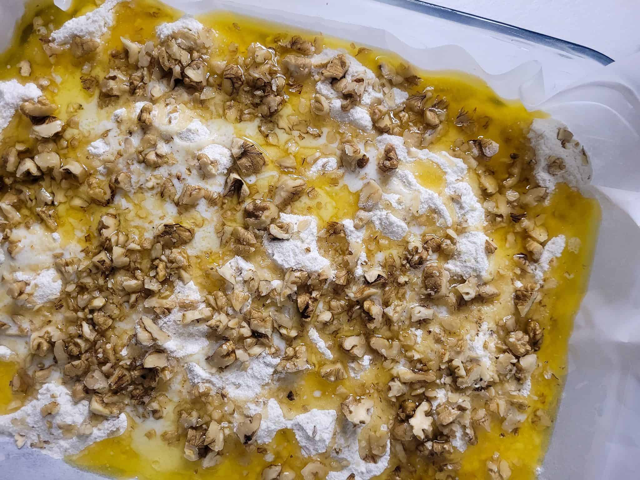 Melted butter with chopped nuts on top of dry cake mix in glass baking dish