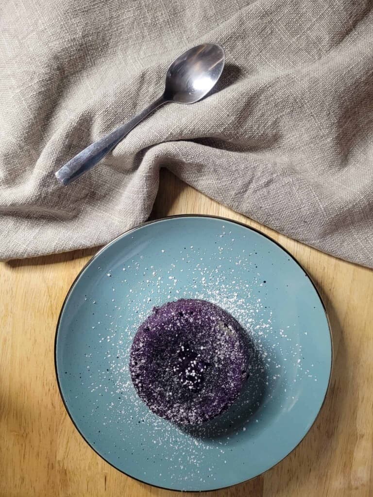 Ube lava cake on a blue plate next to gray towel with a spoon