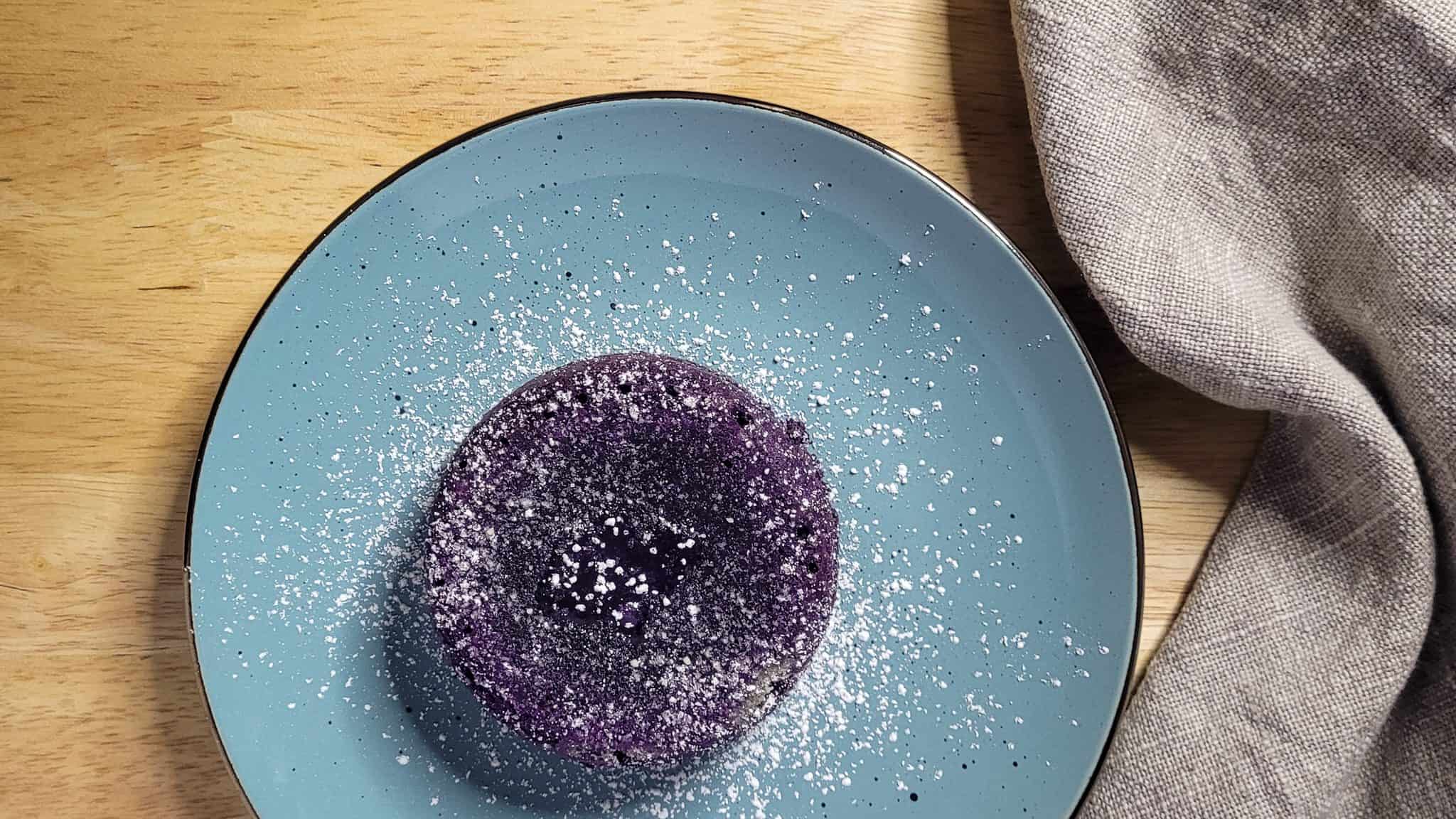 Overhead view of ube lava cake on a blue plate next to a towel