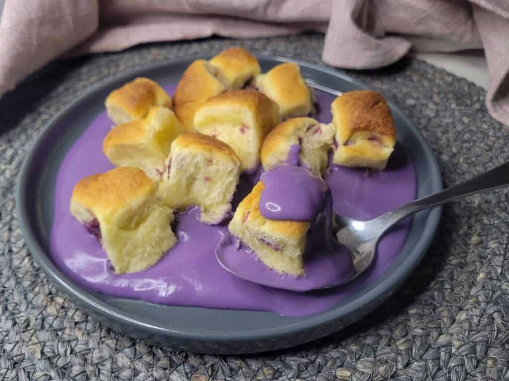 A side view of a gray plate with ube mini buns and ube cream sauce next to pink towel