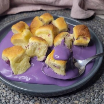 A side view of a gray plate with ube mini buns and ube cream sauce next to pink towel