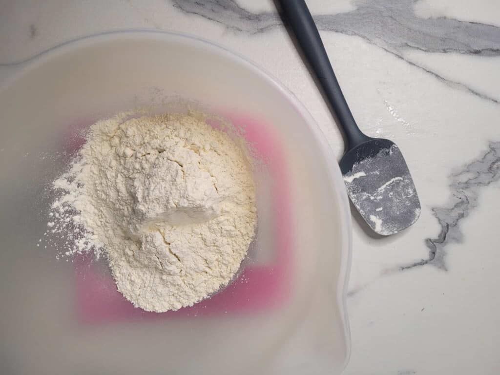 Flour in a plastic bowl next to a silicone spatula