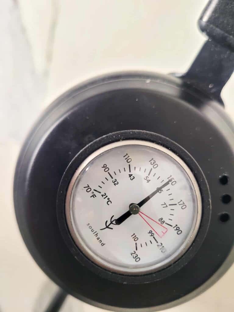 A closeup of a kettle with an attached thermometer on the cover