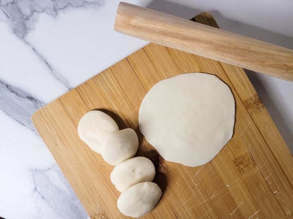 Rolling dumpling wrapper and dough pieces next to a small rolling pin