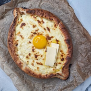 A bread shaped like a boat that has toasted cheese filling in the middle and an egg yolk and slices of butter