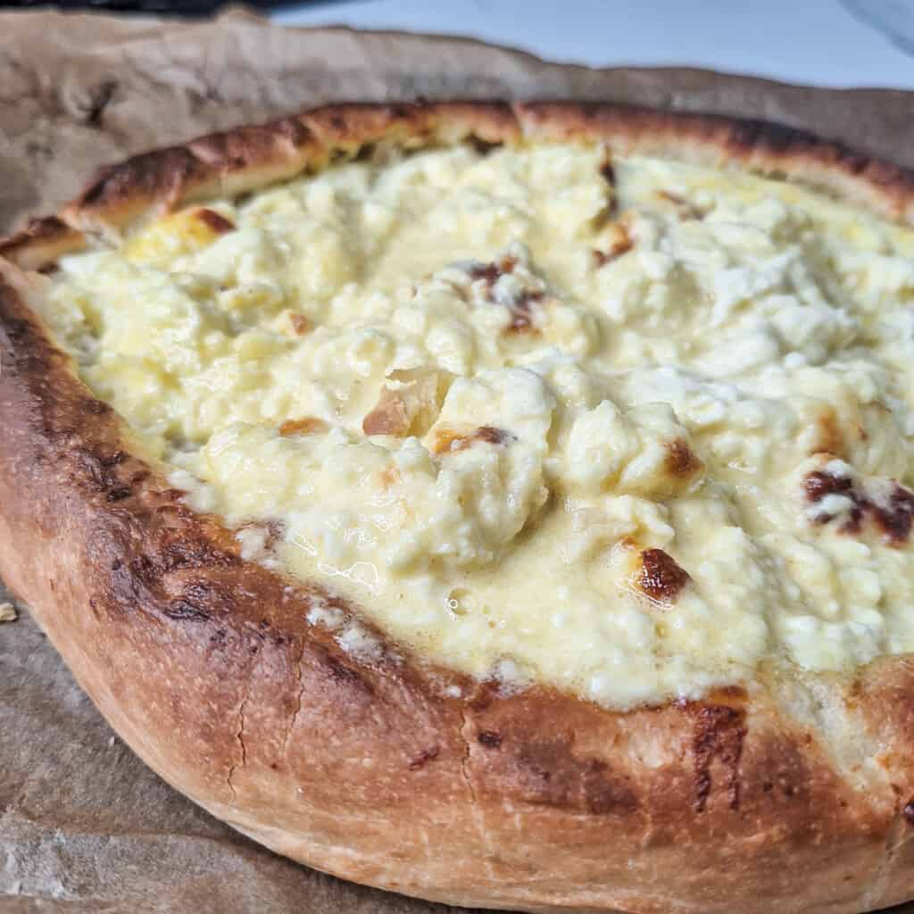 Adjaruli khachapuri or Georgian cheese boat bread with stirred cheese in the middle