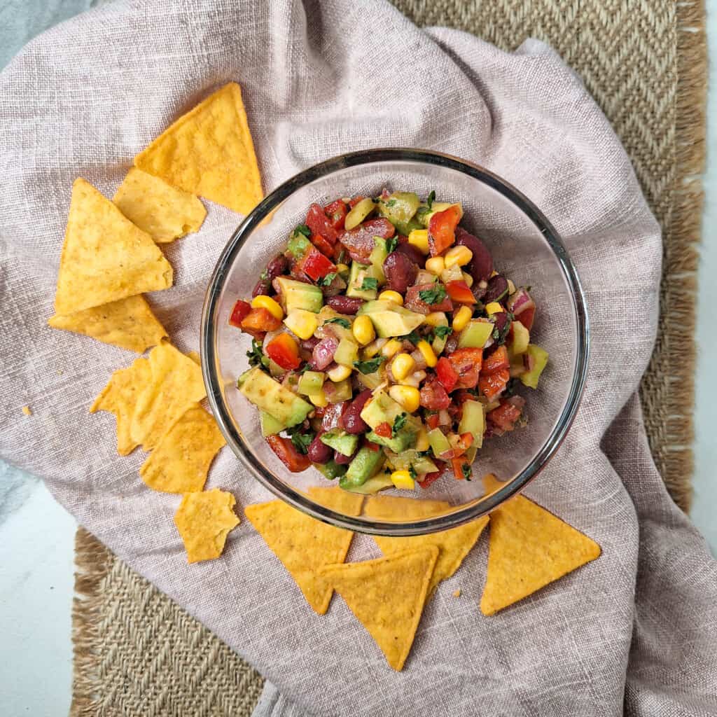 An overhead shot of a bowl of cowboy caviar or corn pico de gallo next to chips