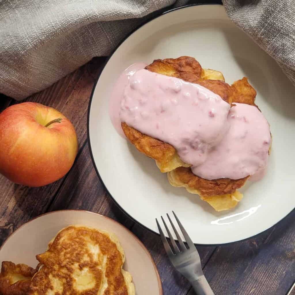 Apple fritters in a shallow bowl topped with pink sour cream