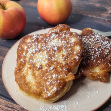 Apple fritters topped with powdered sugar with red apples in the background