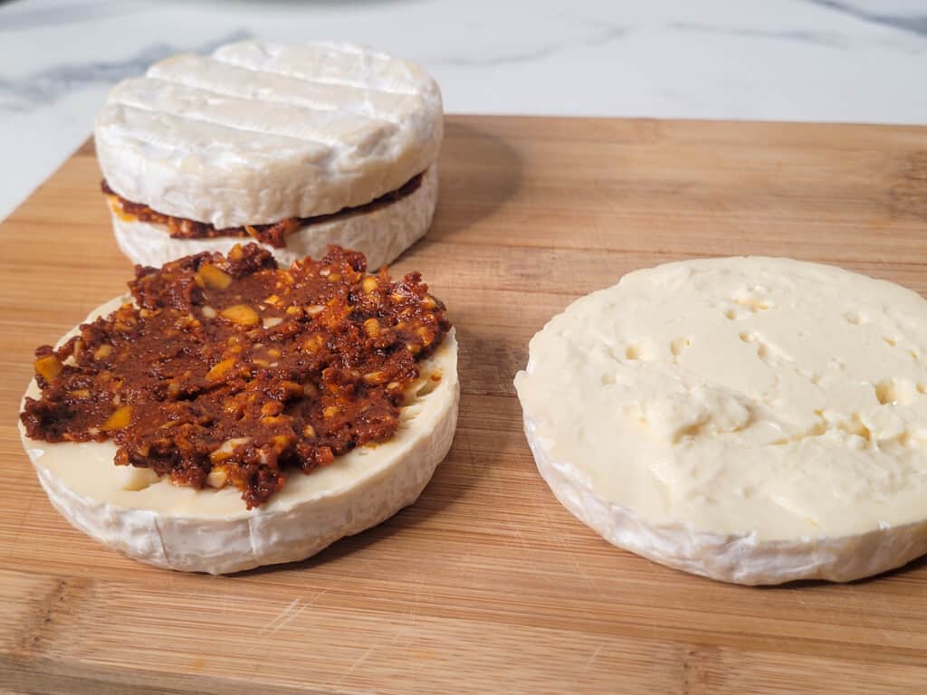 Wheel of cheese sliced in half with spread laid out on a wooden cutting board