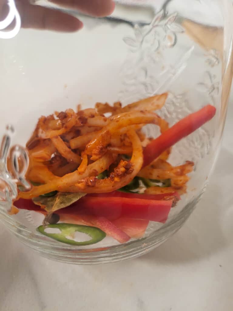 Bottom of a clear jar with marinated onions, vegetables, and other spies