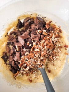 A bowl of banana bread batter with chopped chocolate and pecans