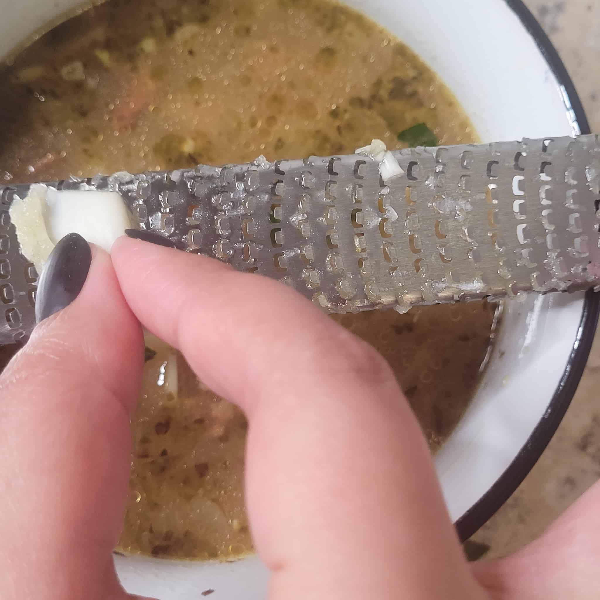 Grated garlic on grater above a bowl of soup