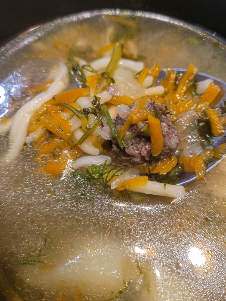 A soup holding up vegetables and meatballs in gupta soup or Georgian meatball soup