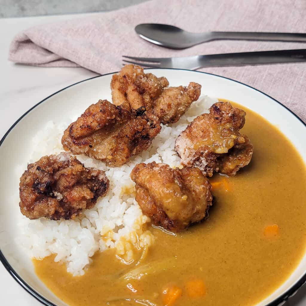 A plate of Japanese curry and fried chicken next to a spoon and fork