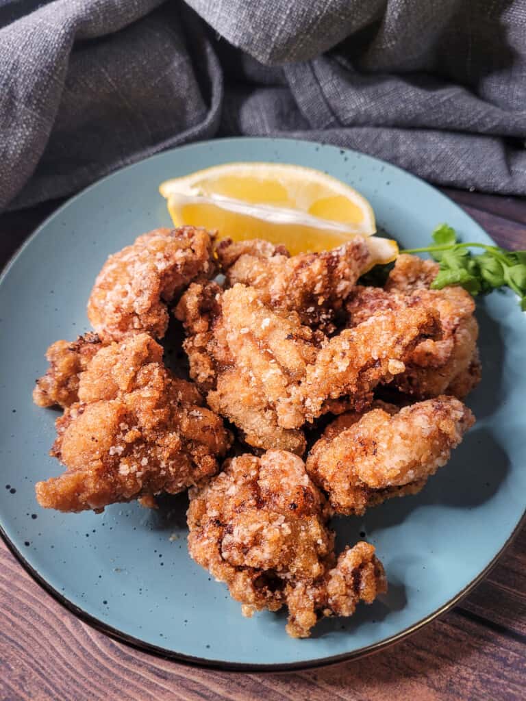 Japanese fried chicken on a blue plate with parsley and lemon wedges