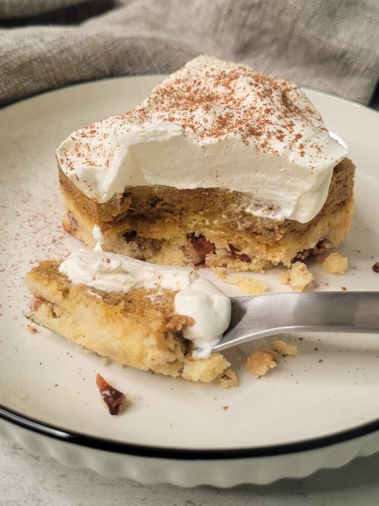 A slice of pumpkin crunch cake with whipped cream and fork on a white plate