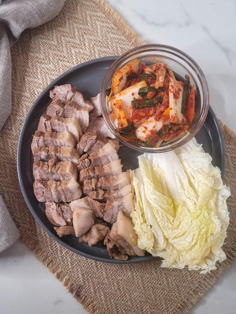 Overhead shot of a plate with boiled pork belly, salted cabbage and fresh kimchi