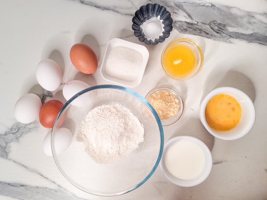 Eggs, melted butter, sugar and other ingredients next to a bowl of flour.