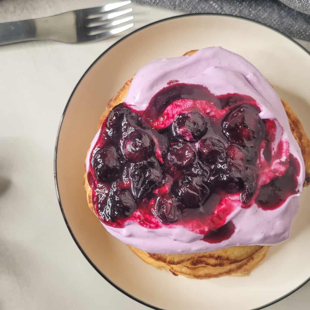 Blueberry pancakes with blueberry sauce in a plate next to a fork