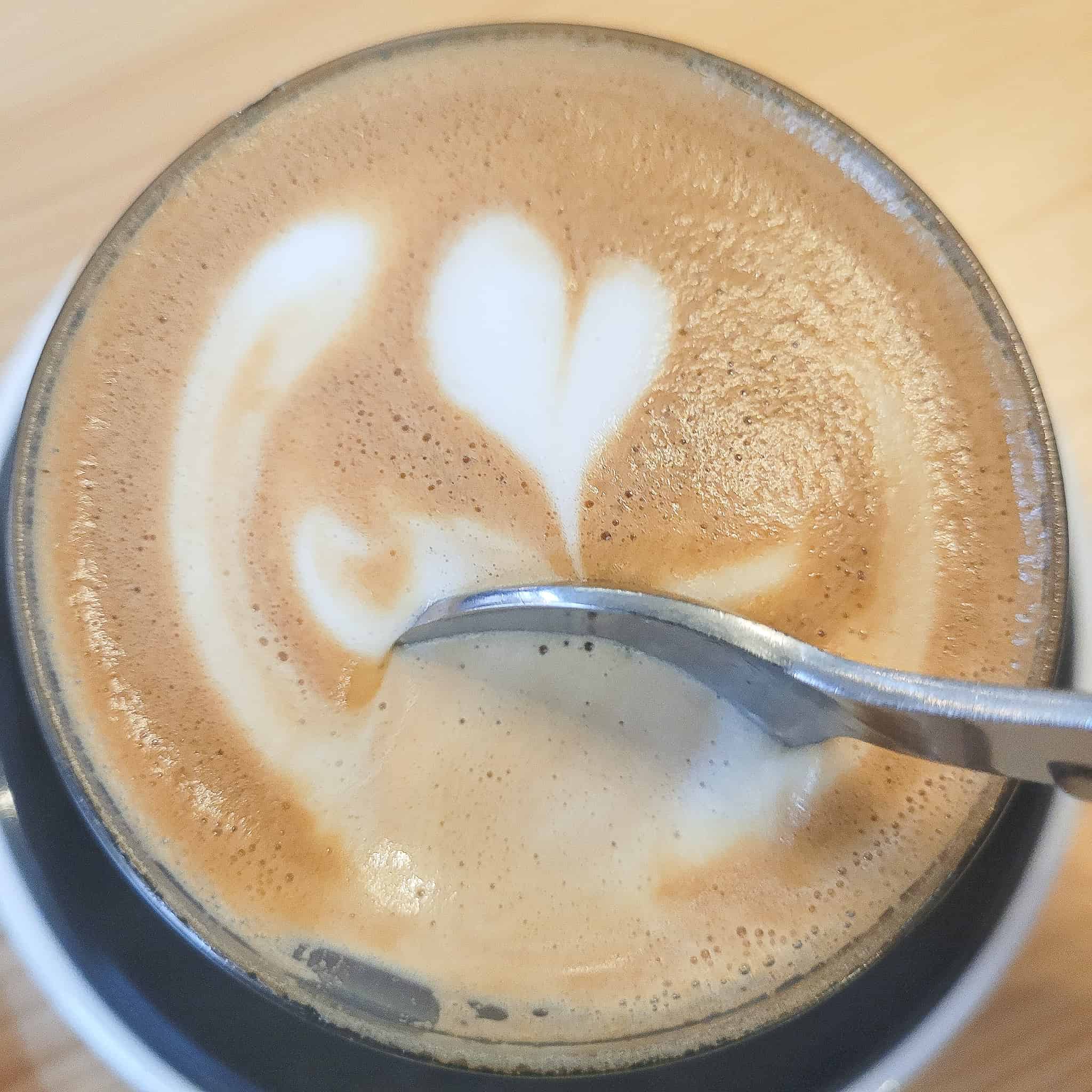 Spoon pushing aside foam on a cortado 