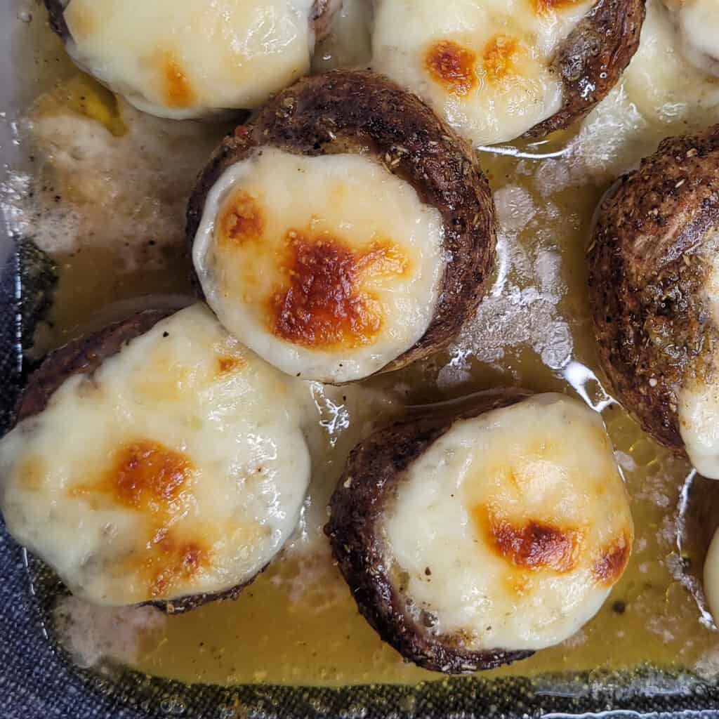 Closeup of melted cheese stuffed in mushrooms roasted in a pan