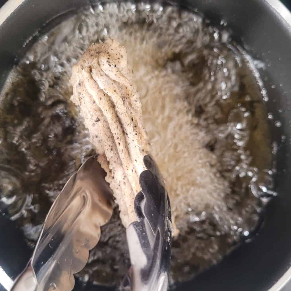 Frozen black sesame churros dropped into a pot of oil
