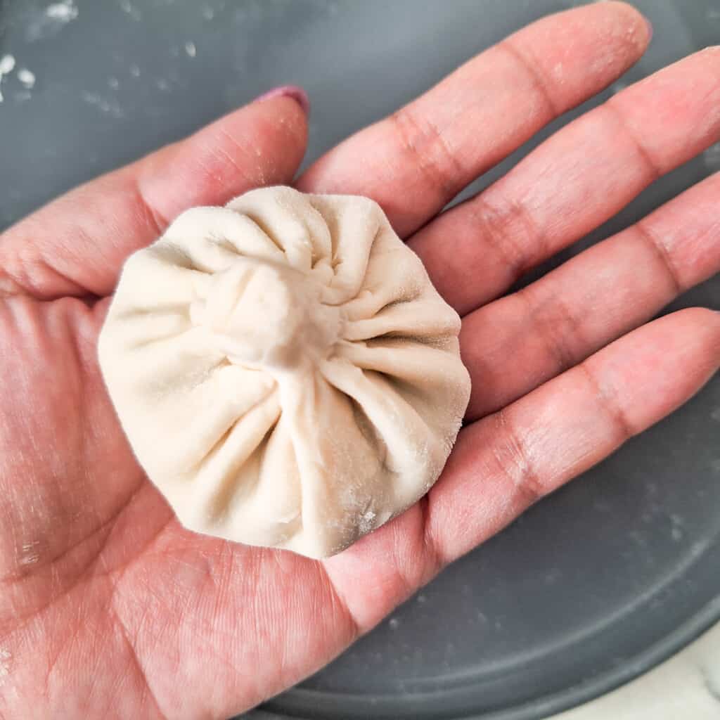 A hand holding a folded khinkali