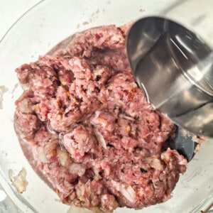 A half cup of water poured into a mixed minced meat in a glass bowl