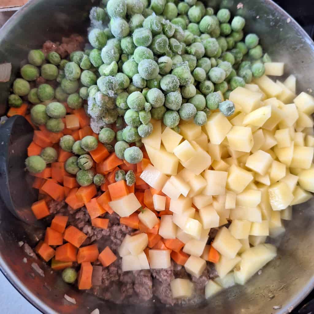 Raw vegetables and frozen peas on top of minced meat in a pot