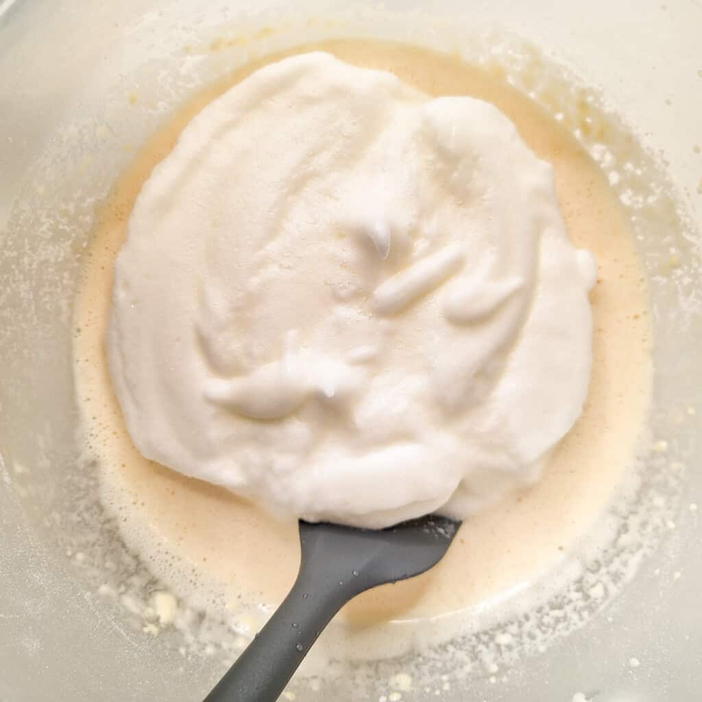 Pancake batter with fluffy egg whites on top in a bowl with a gray spatula