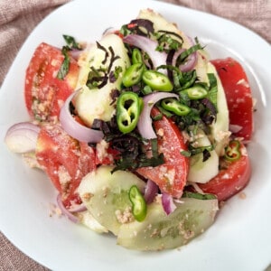 Closeup of Georgian cucumber tomato salad topped with chopped chilies and purple basil in a white bowl