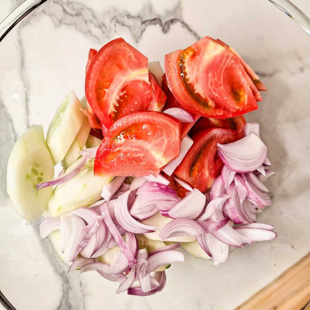 sliced tomatoes, cucumbers, and onions for Georgian cucumber tomato salad in a glass bowl