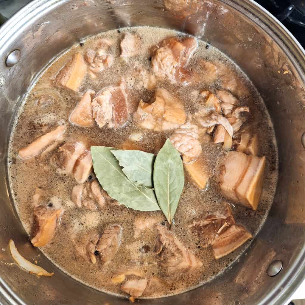 Meat pieces in a dark marinade sauce with bay leaves in the process of cooking inside a stockpot