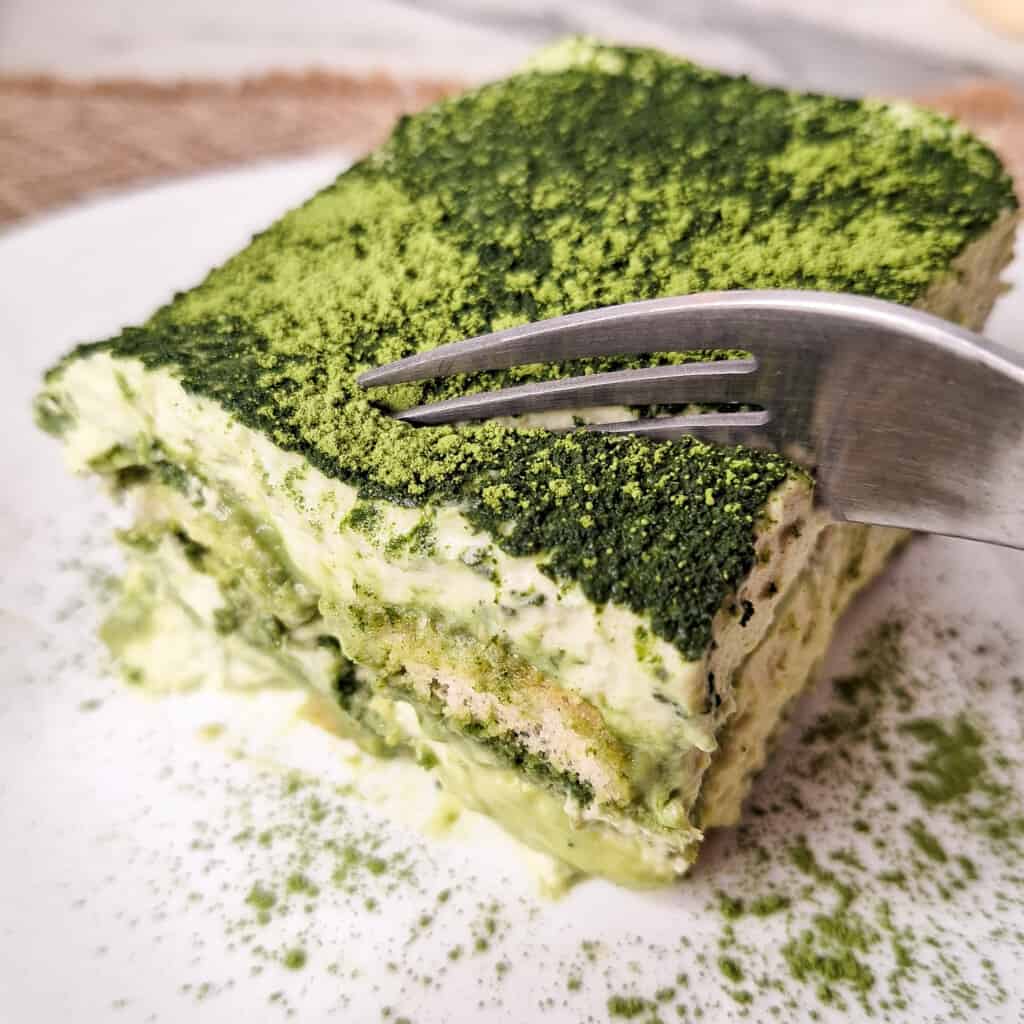 Silver fork slicing through a square of matcha tiramisu