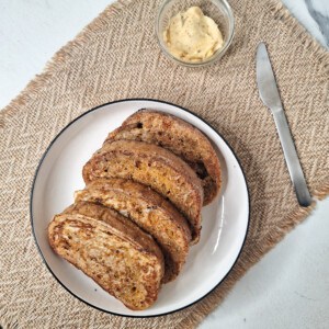 Georgian egg bread, or kikliko, in a round white plate on a brown platemat next to silver knife