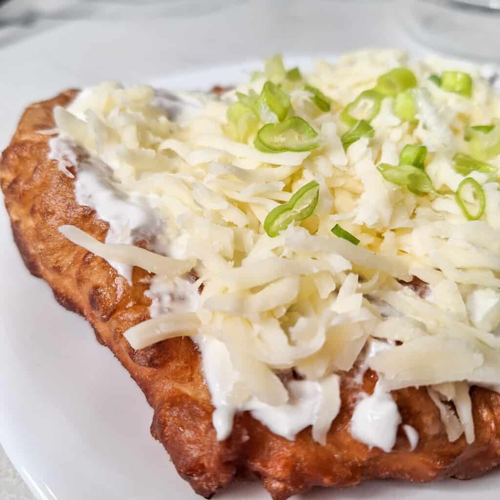 Closeup of langos or Hungarian deep fried bread with a topping of sour cream, cheese, and green onions