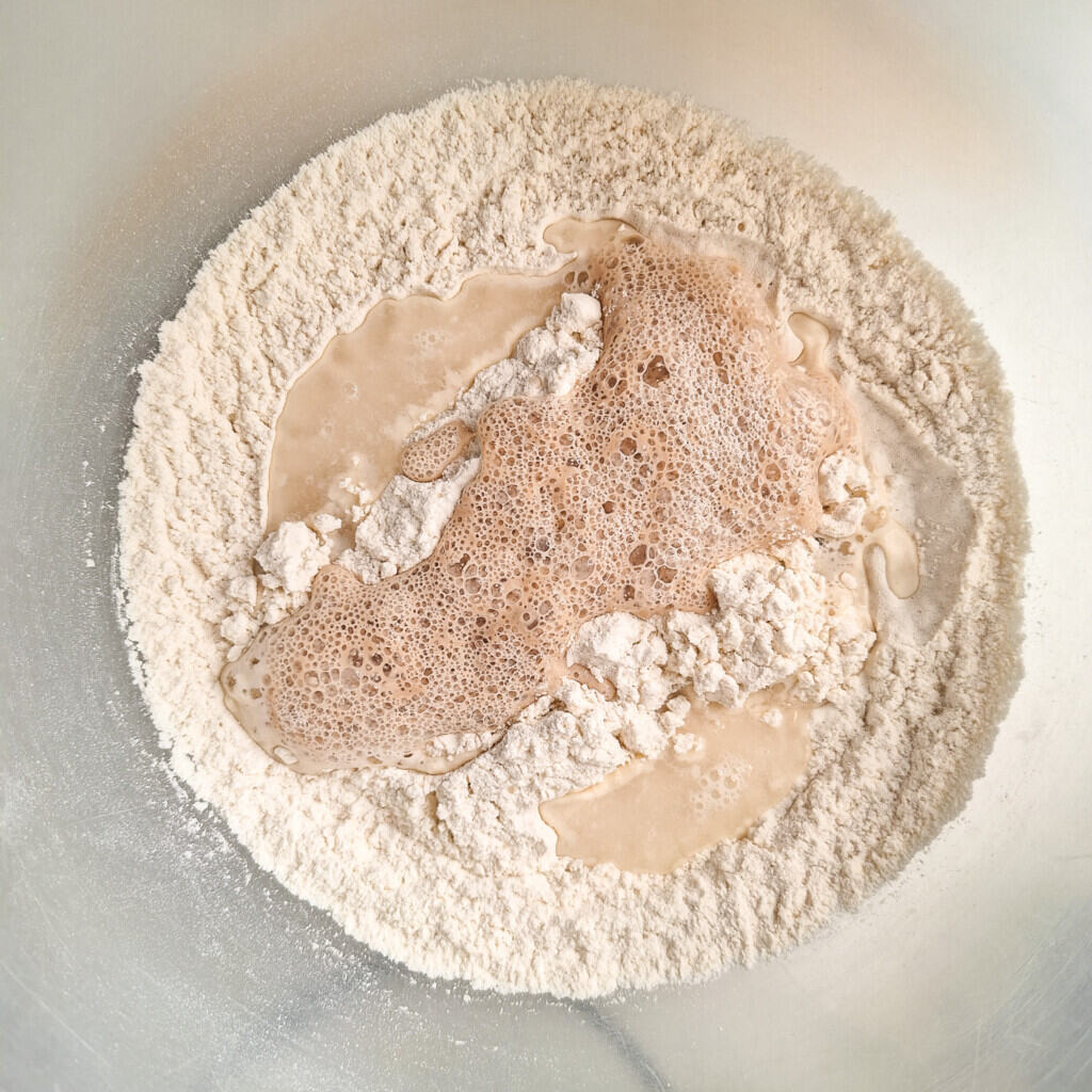 Flour in a bowl topped with bloomed yeast and water